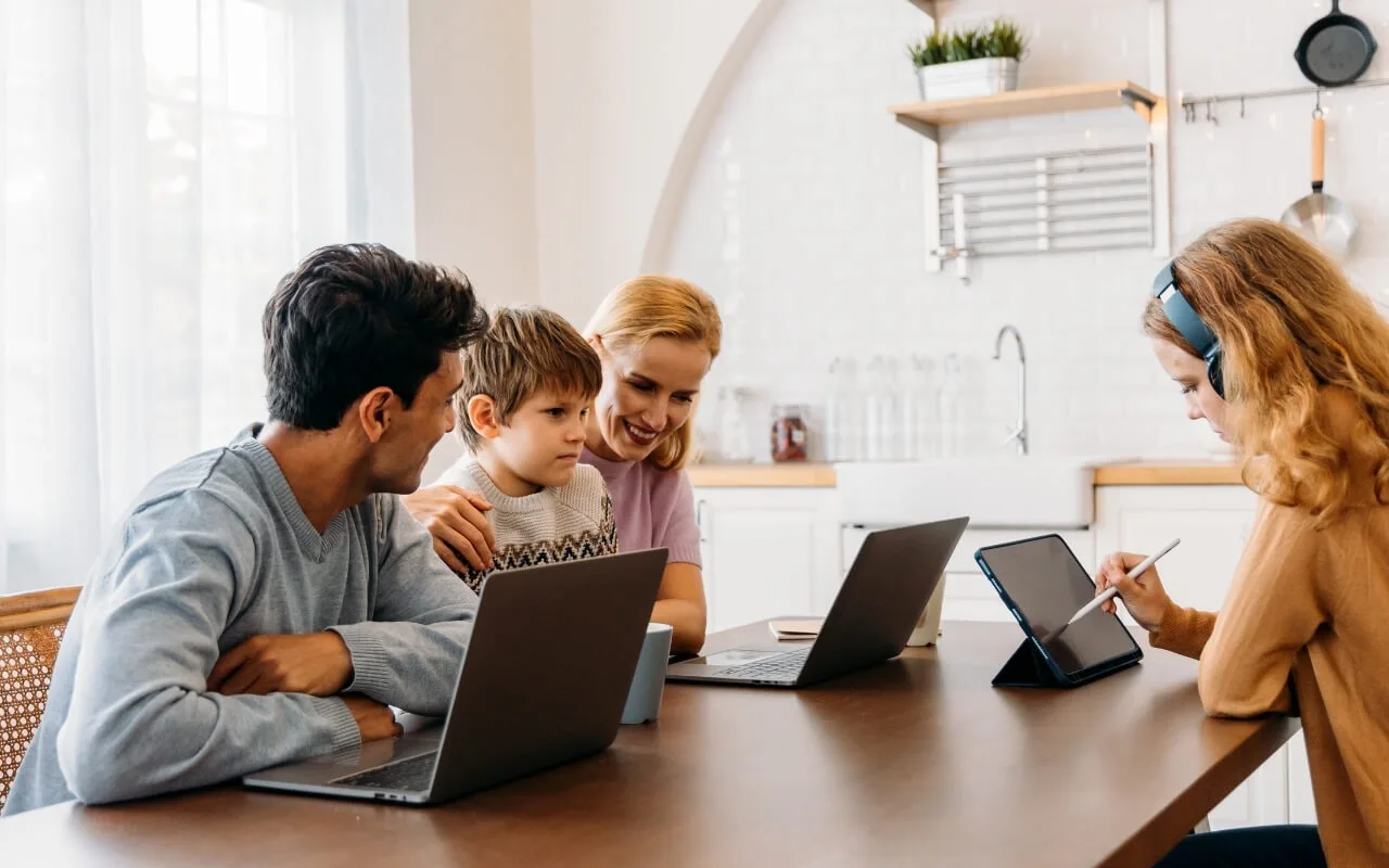 Family using laptops and tablet in kitchen workspace.